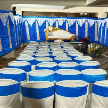 Tent rental service set up by Dream Tent House in Bangalore, featuring a decorated space with white chairs covered in elegant blue and white fabric, and a luxurious sofa against a backdrop of blue and white drapes, creating a festive and inviting atmosphere.